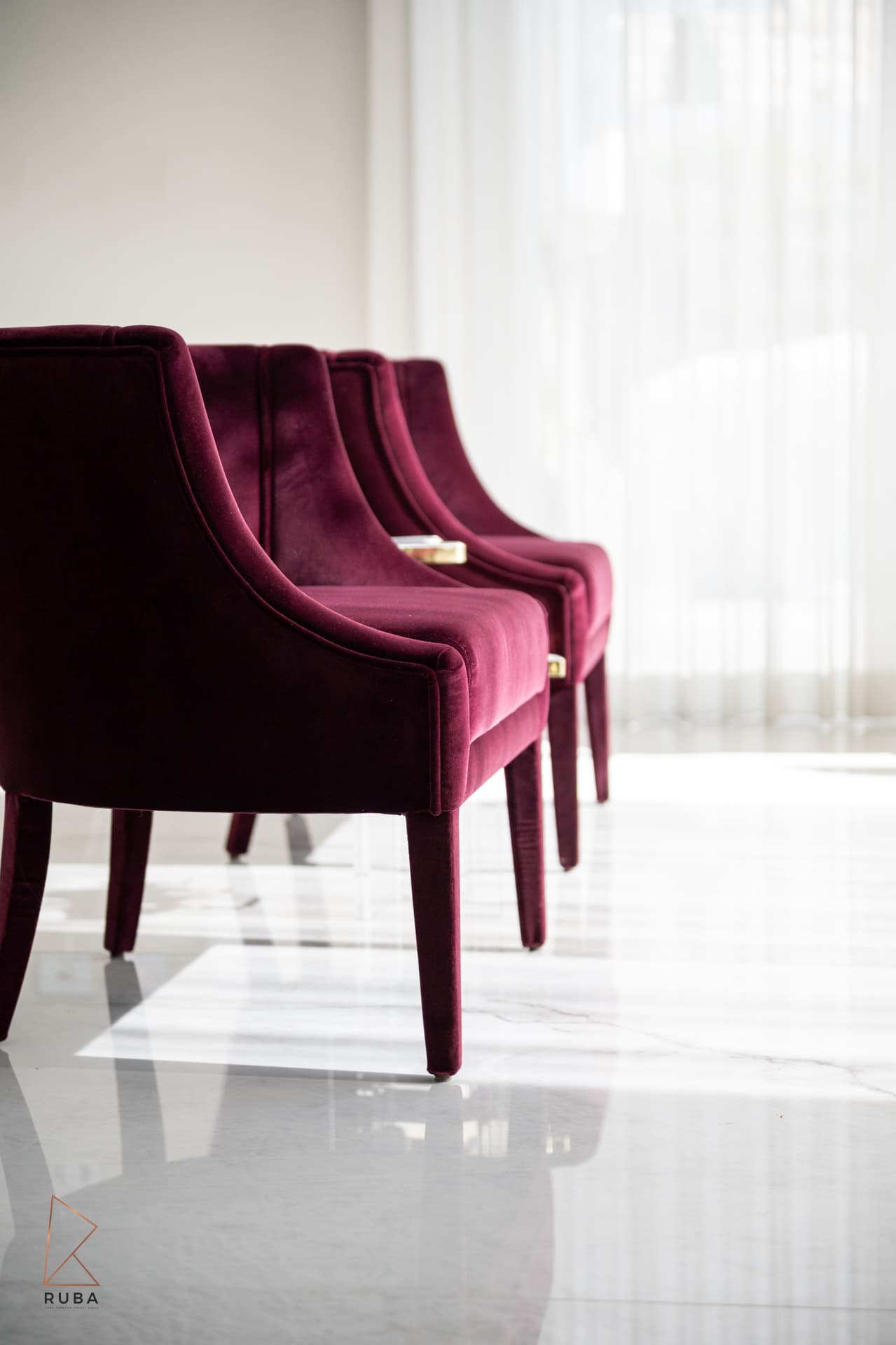 Burgundy velvet dining chairs with gold arm detail on marble
