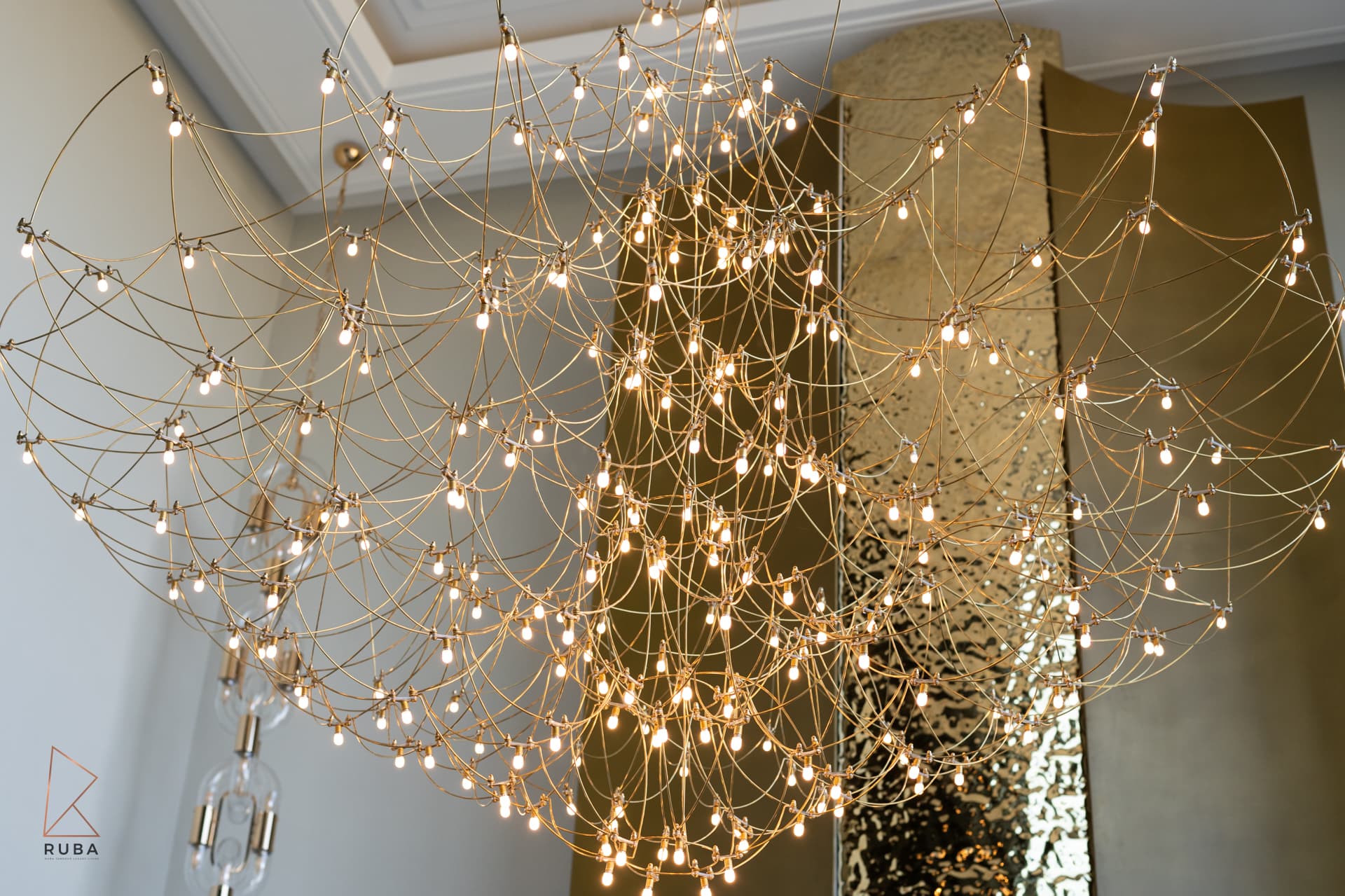 Spiderweb crystal chandelier on gold wire against gold tree sculpture