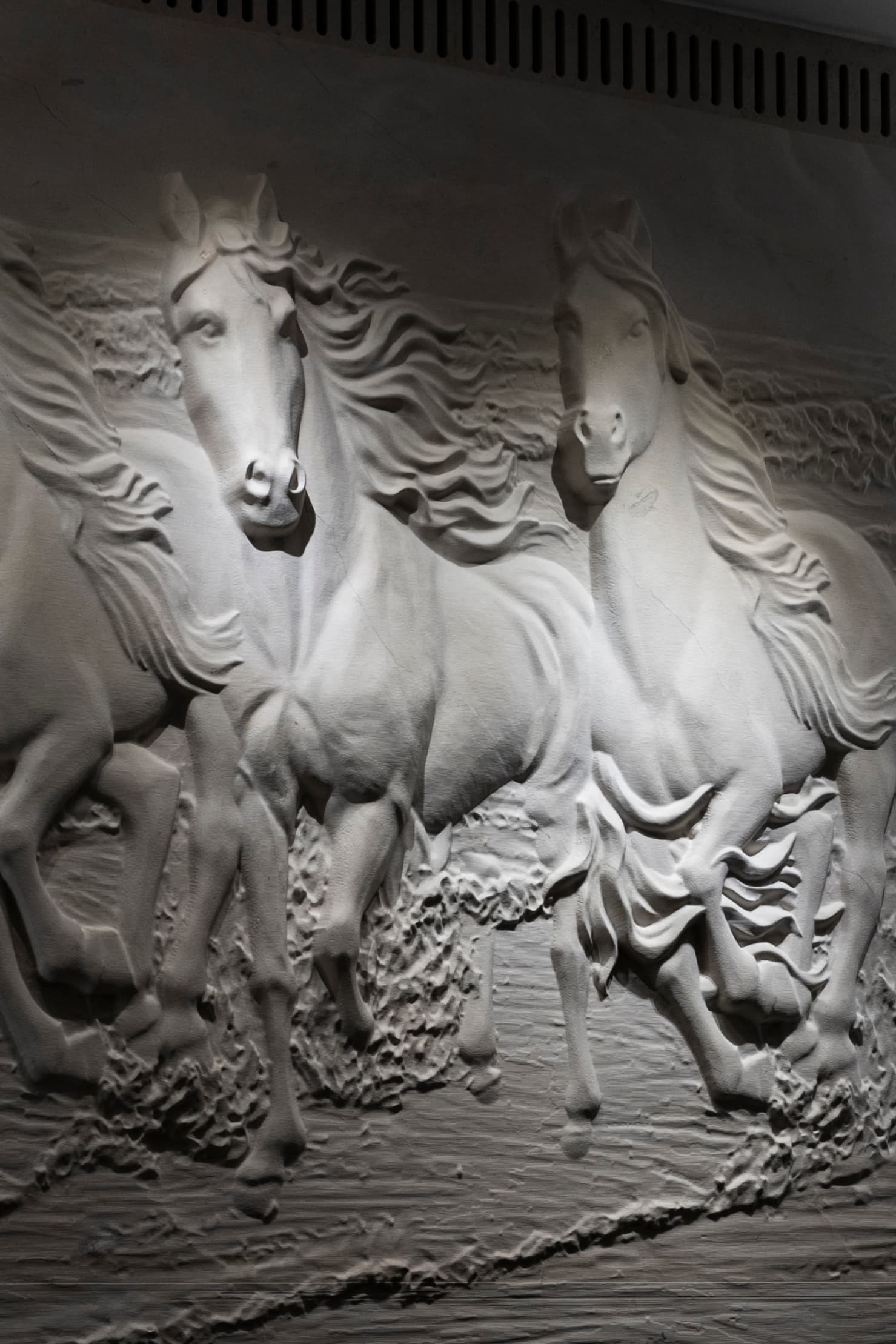 Hand-sculpted galloping horses in white plaster relief — close-up