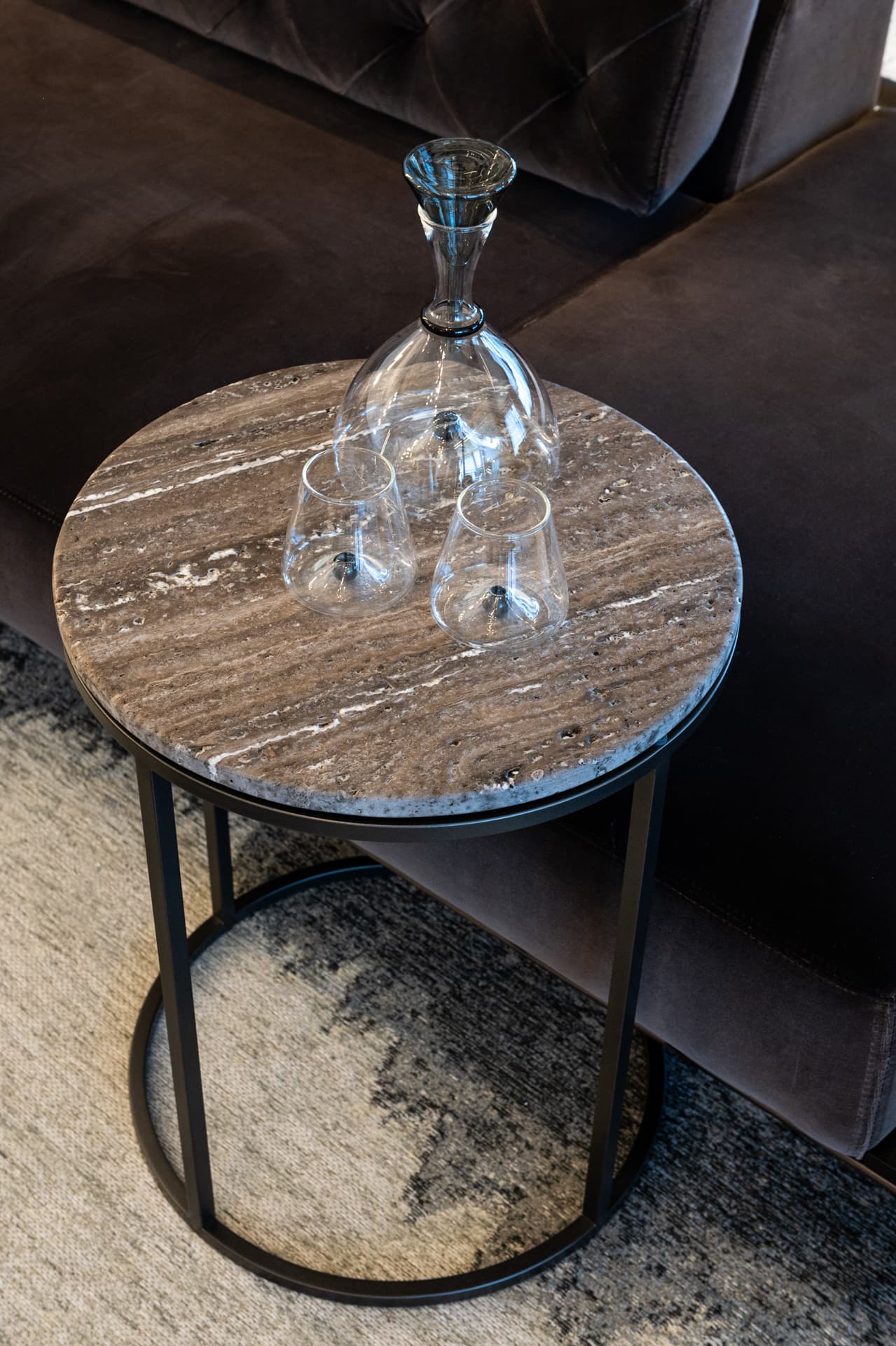 Round travertine side table with crystal decanter on black steel base