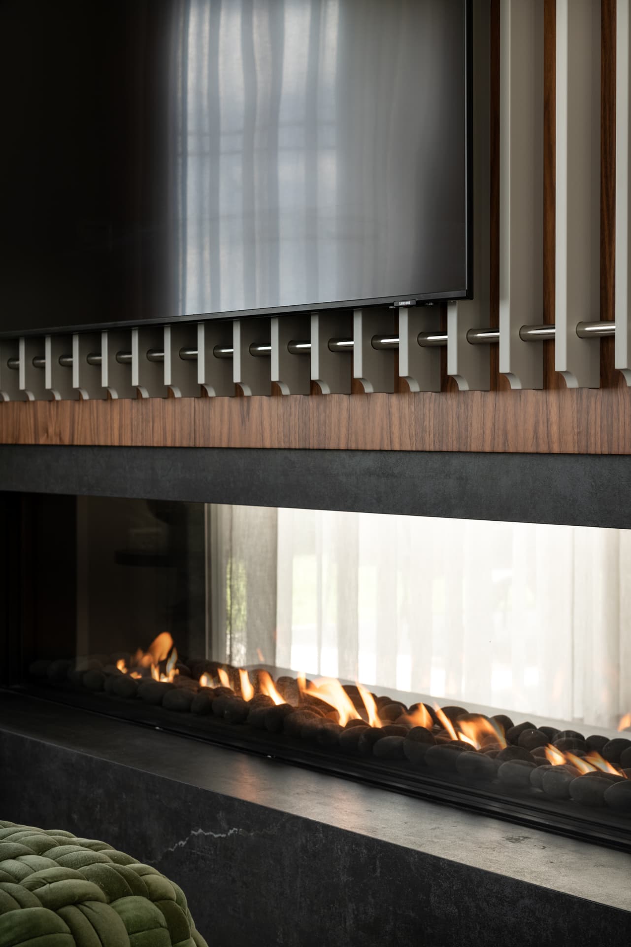 Vertical walnut slat screen behind three-sided gas fireplace